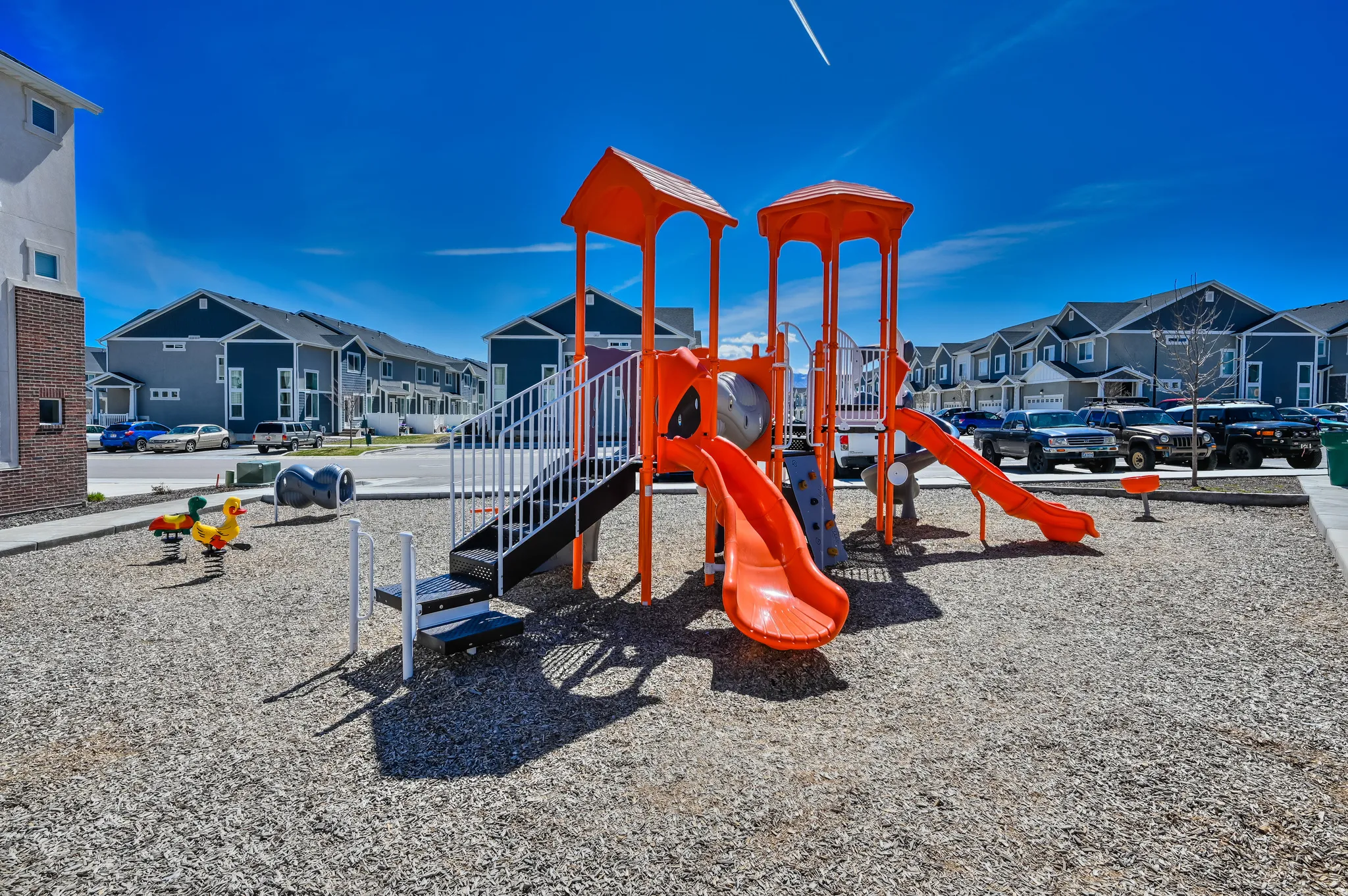 Community playground featuring an orange play structure with multiple slides and climbing elements