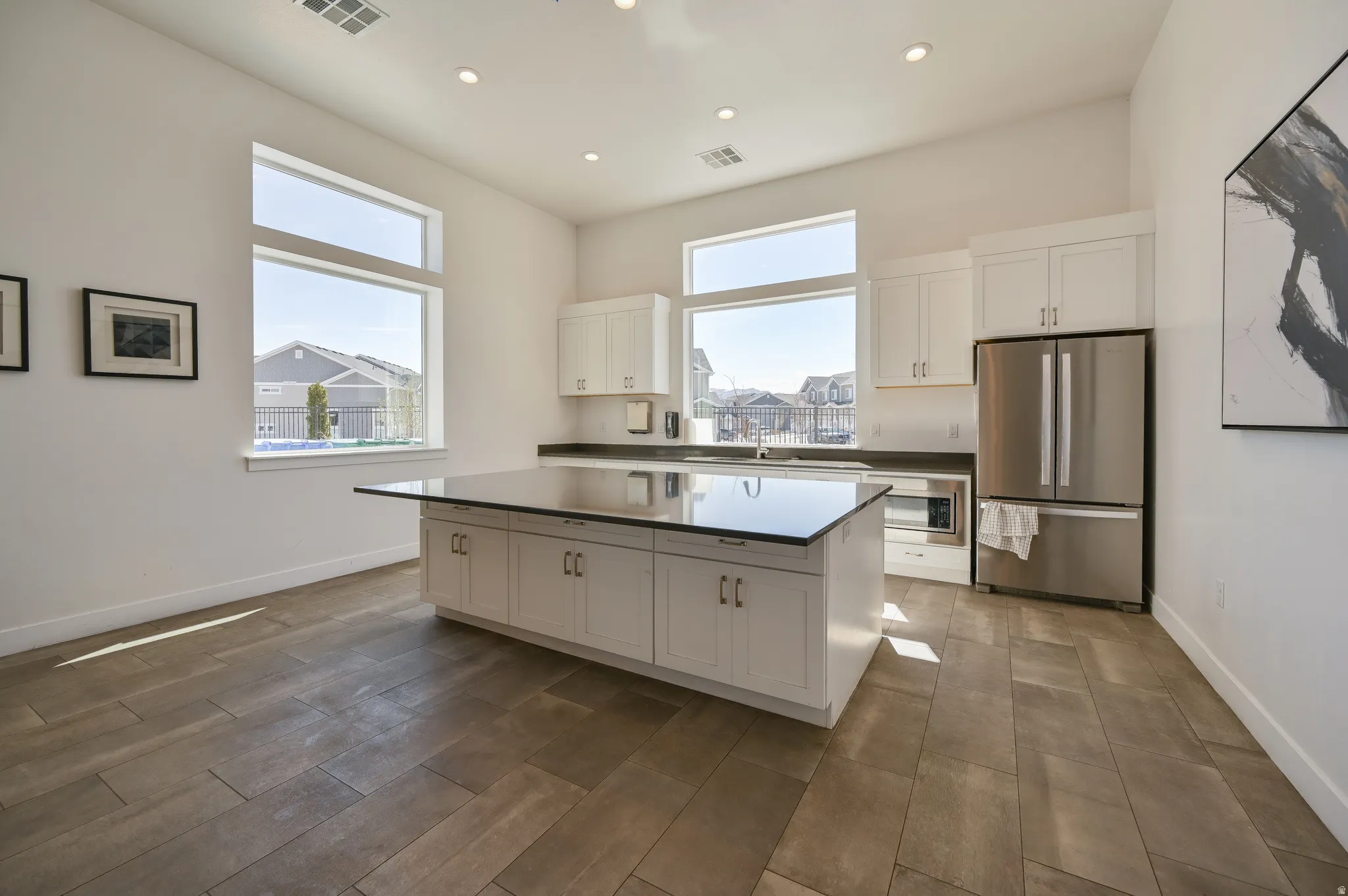 Spacious kitchen featuring a large central island with a dark countertop, white shaker-style cabinetry, stainless steel appliances, and wood-finish flooring