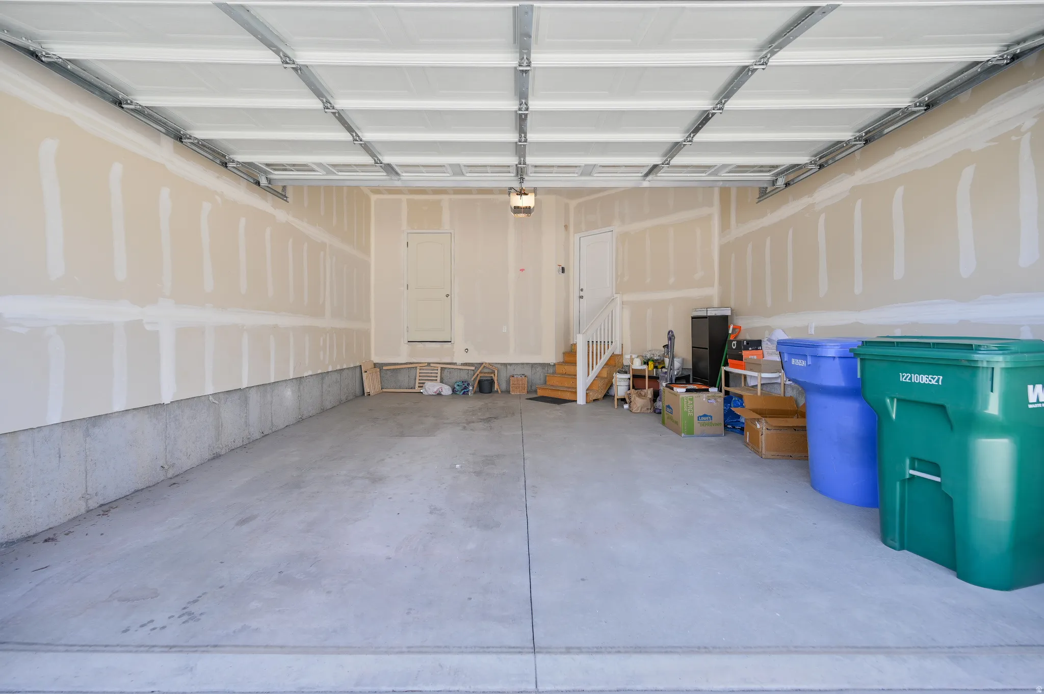 Spacious garage featuring a concrete floor, exposed ceiling joists, and a partial staircase with white railing