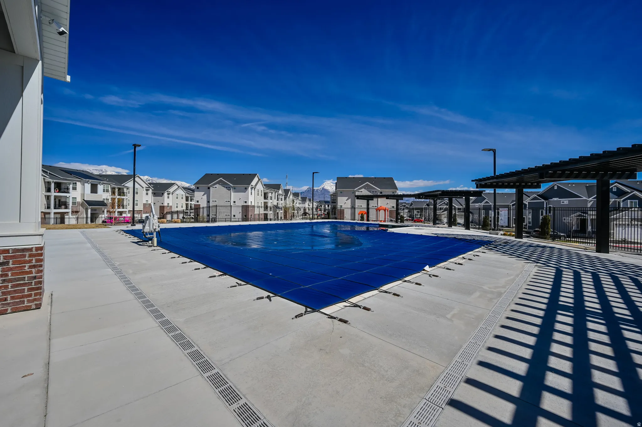 Expansive outdoor pool area featuring a large, covered pool, concrete decking, multiple shade pergolas, and decorative iron fencing