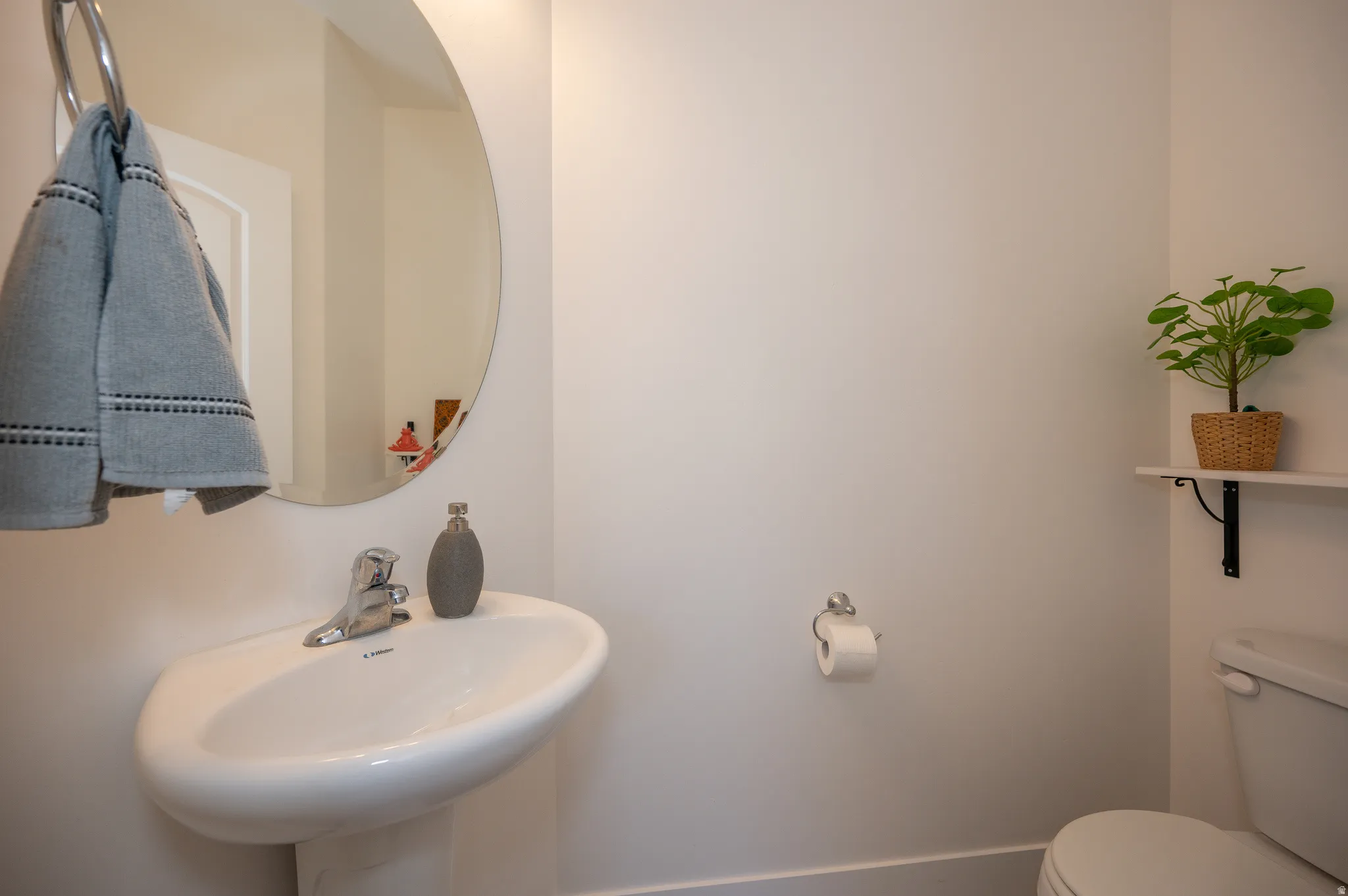 Pedestal sink with chrome faucet, circular wall mirror, and white toilet