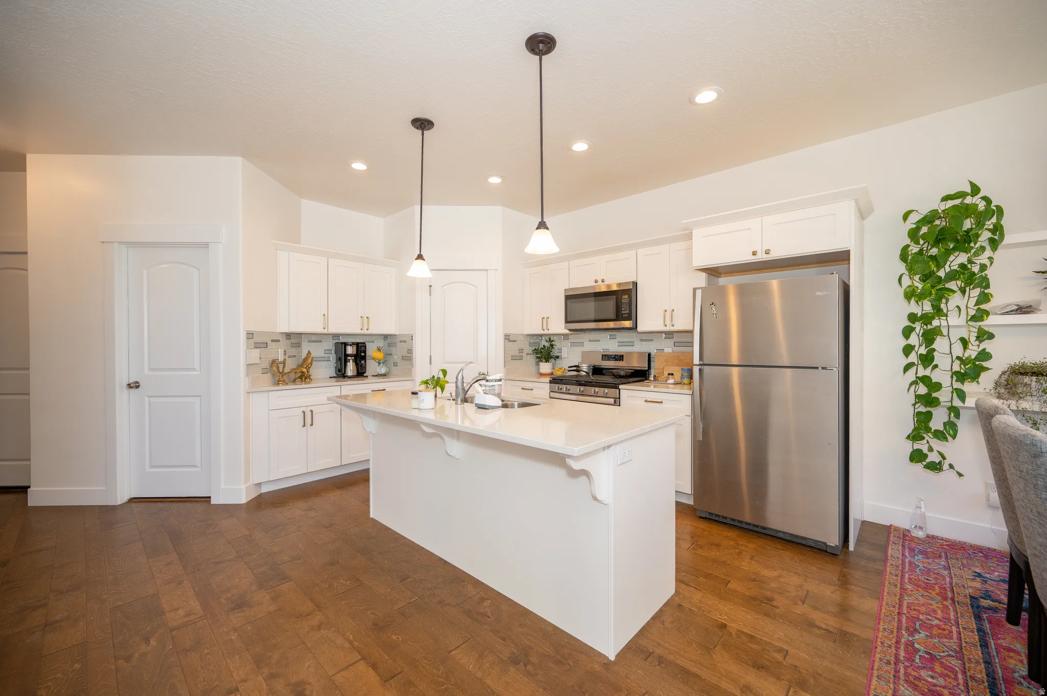 Kitchen featuring a central island with countertop seating, white cabinetry, stainless steel appliances, and wood-finish flooring