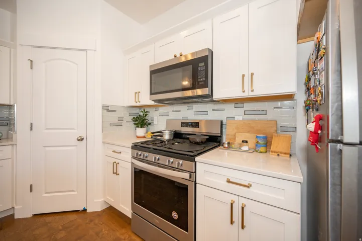 Modern kitchen with white shaker cabinetry, stainless steel appliances, quartz countertops, and a contemporary tile backsplash