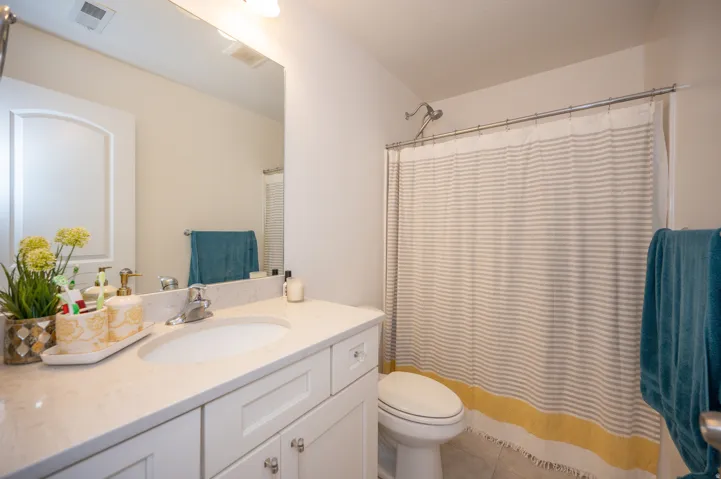 Bathroom featuring a white vanity with an integrated sink and light-toned countertop, a frameless wall mirror, and a shower with a chrome showerhead