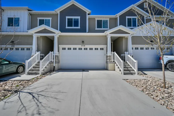 Modern townhome exterior featuring an attached two-car garage, covered entry with balustrade railings, and decorative stone accents