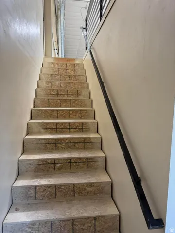 Staircase with exposed OSB treads and risers, featuring a black metal handrail