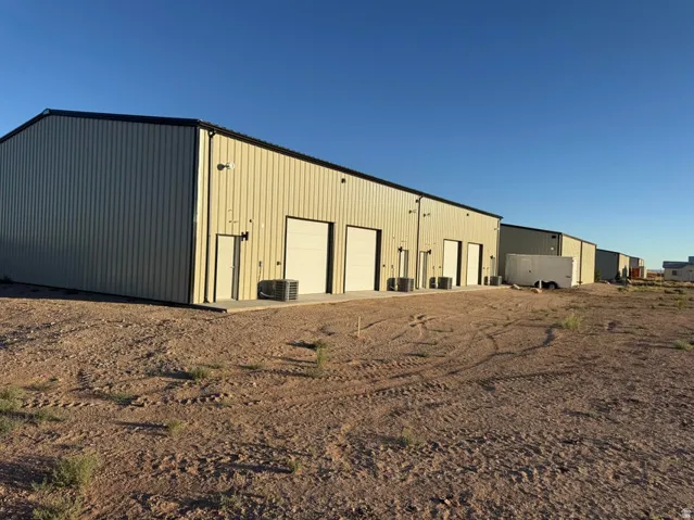 Multi-unit commercial building featuring light-colored metal siding, multiple roll-up garage doors, pedestrian entry doors, and individual HVAC units
