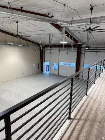 Spacious commercial interior featuring a mezzanine with black metal railings, exposed ductwork, large ceiling fans, and overhead lighting