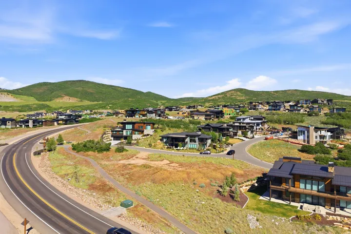 Modern residential properties situated on a hillside with natural landscaping, featuring a paved road and clear skies