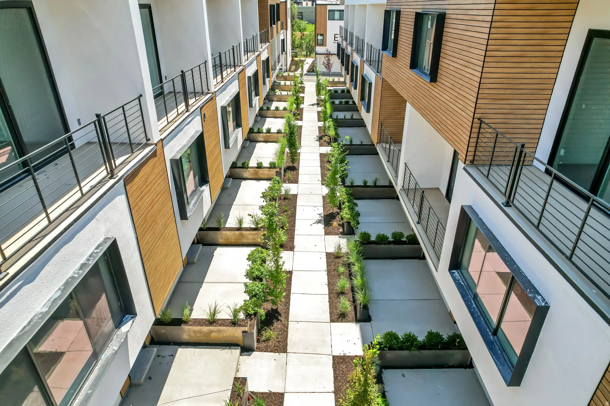 Modern multi-level townhome exteriors featuring white stucco, natural wood-finish siding, and large dark-framed windows