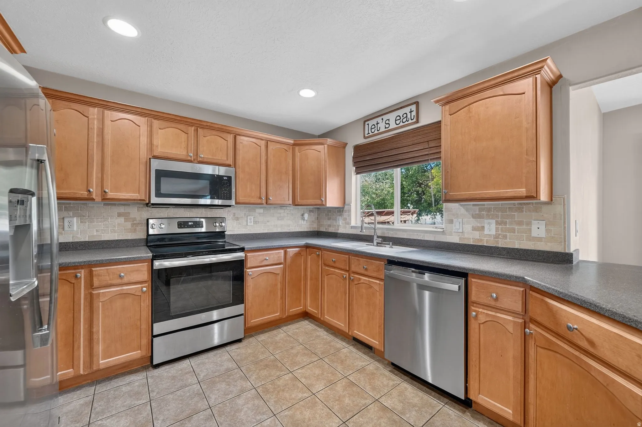 Kitchen featuring warm wood cabinetry, stainless steel appliances, speckled countertops, and a tiled backsplash