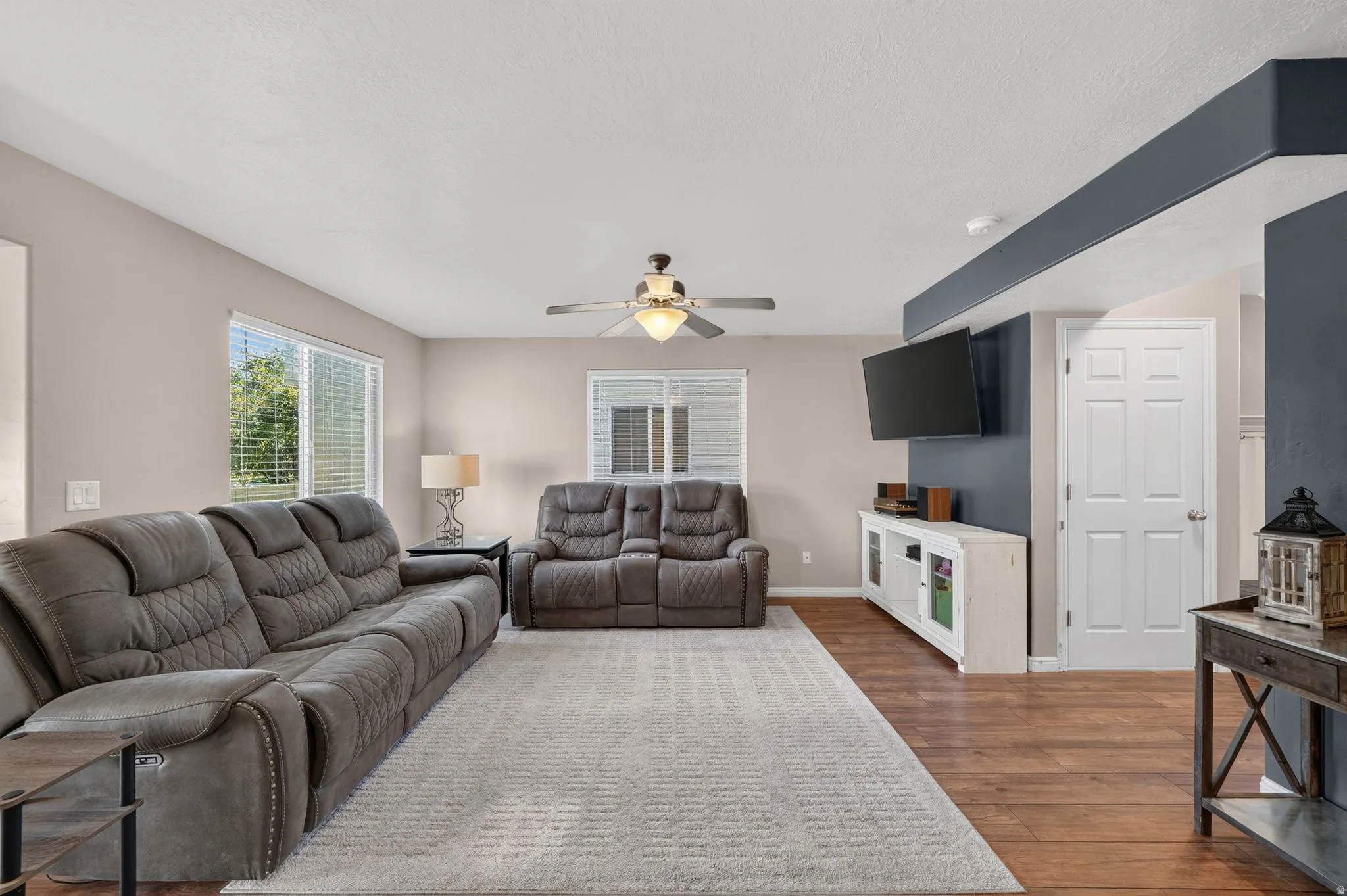 Spacious living area featuring light neutral wall tones, wood-finish flooring, and a ceiling fan with integrated lighting