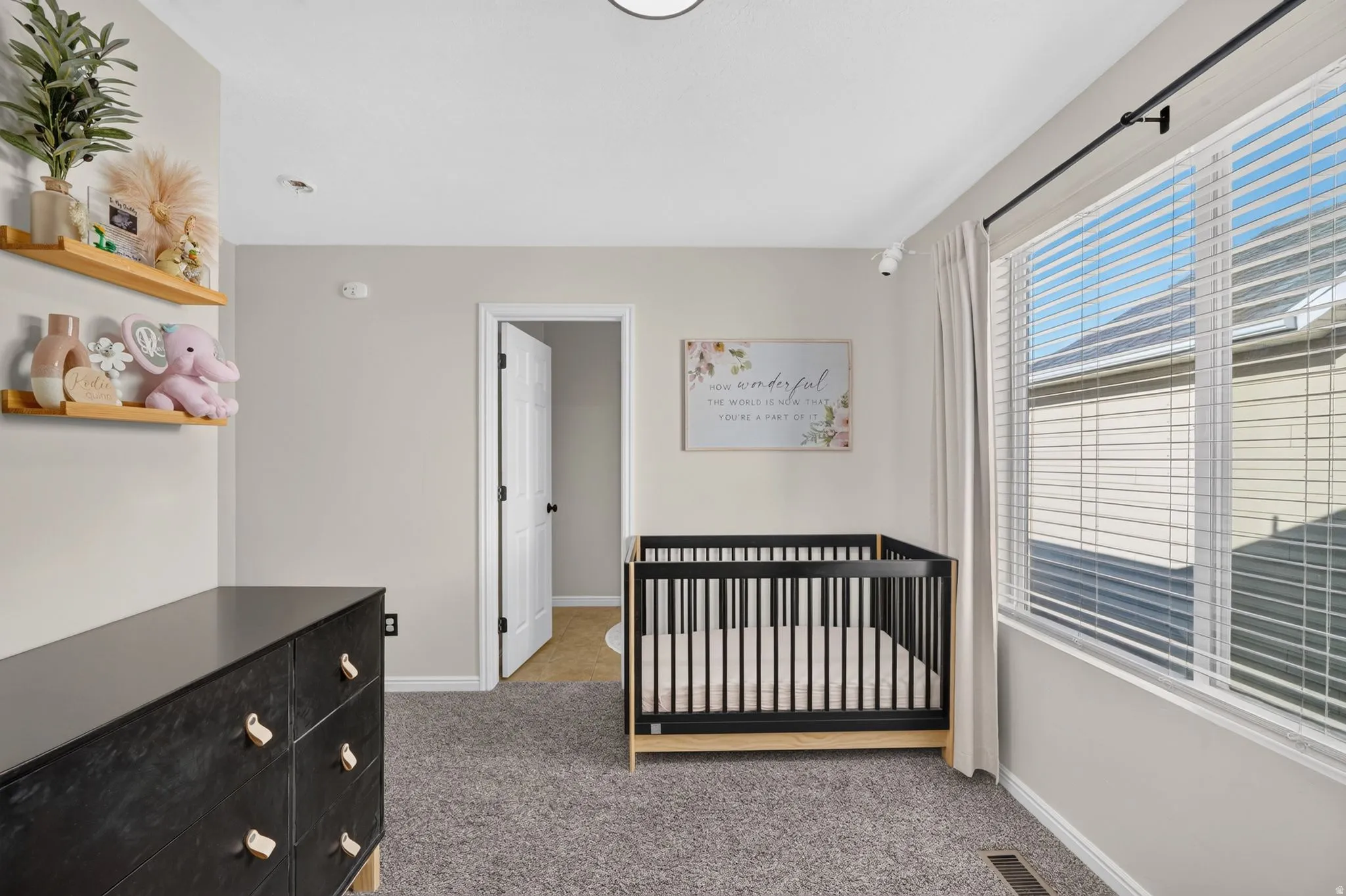 Carpeted room featuring neutral wall tones, a large window with blinds, and a standard door frame