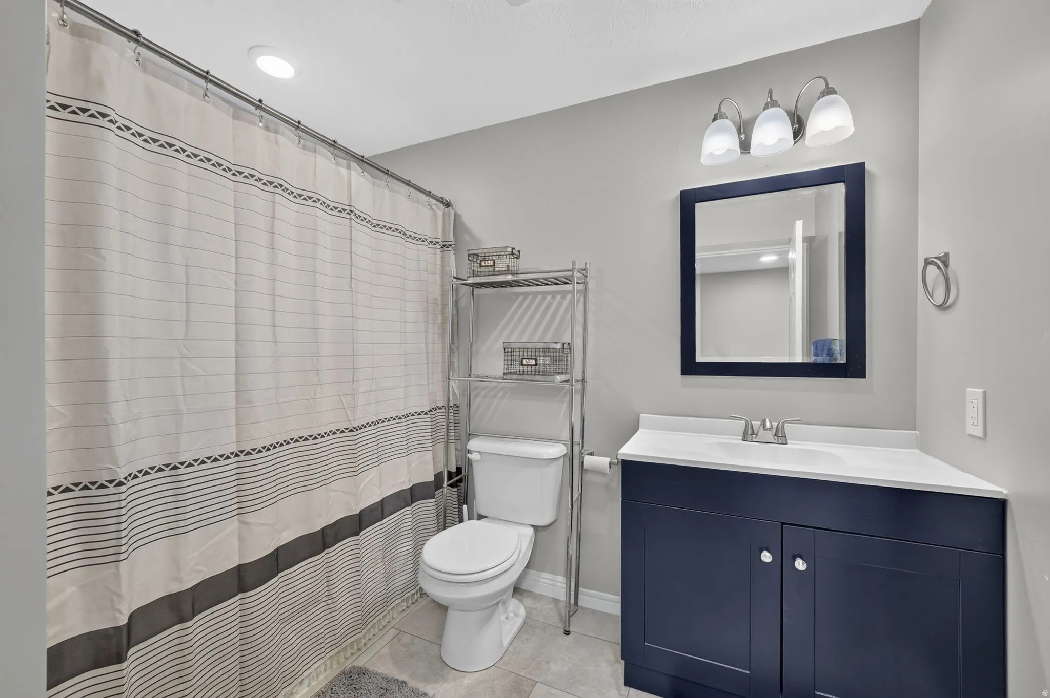 Bathroom featuring a dark blue vanity with a white countertop and integrated sink, a rectangular mirror with a dark blue frame, a three-light vanity fixture, and light gray wall paint