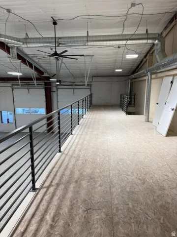 Mezzanine level featuring durable composite wood flooring, modern horizontal metal railings, industrial-style ceiling with exposed ductwork, multiple recessed lighting fixtures, and an oversized ceiling fan