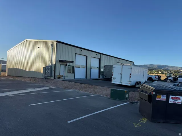 Industrial building featuring corrugated metal siding, multiple roll-up bay doors, and a paved parking area with marked spaces