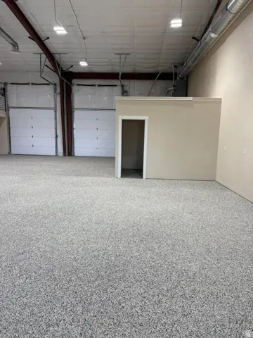 Spacious industrial interior featuring a durable speckled epoxy floor, two large overhead doors, exposed ductwork, and a partial height interior wall with doorway