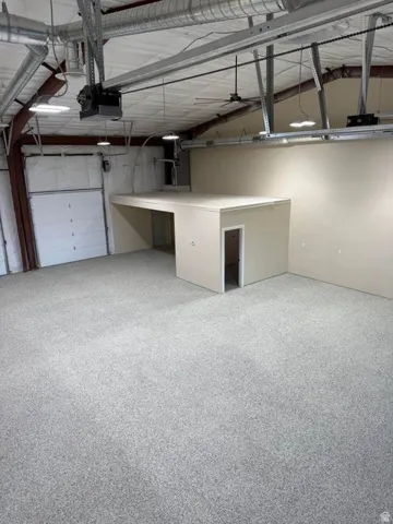 Spacious commercial interior featuring a mezzanine level, high ceilings with exposed ductwork, multiple overhead lighting fixtures, and a roll-up door