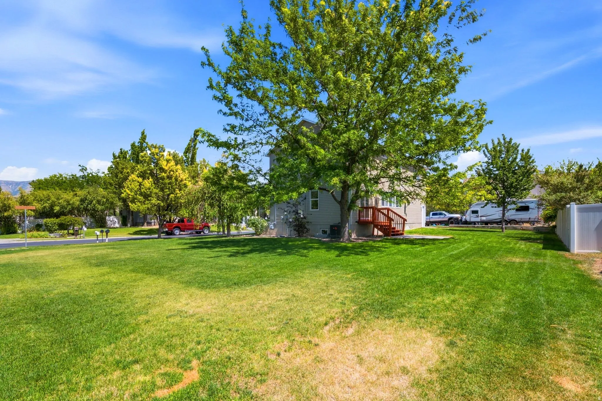 Expansive grass lawn with mature trees and a rear deck featuring red-stained wood