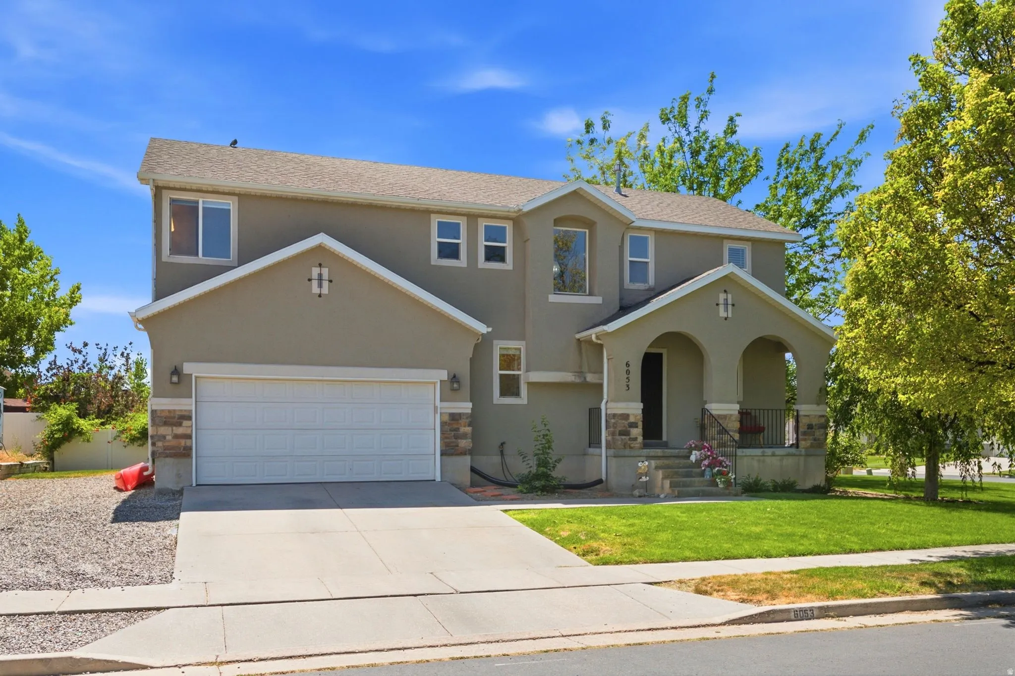 Stucco exterior home featuring an attached two-car garage, covered entry porch with arched openings, stone veneer accents, and a concrete driveway