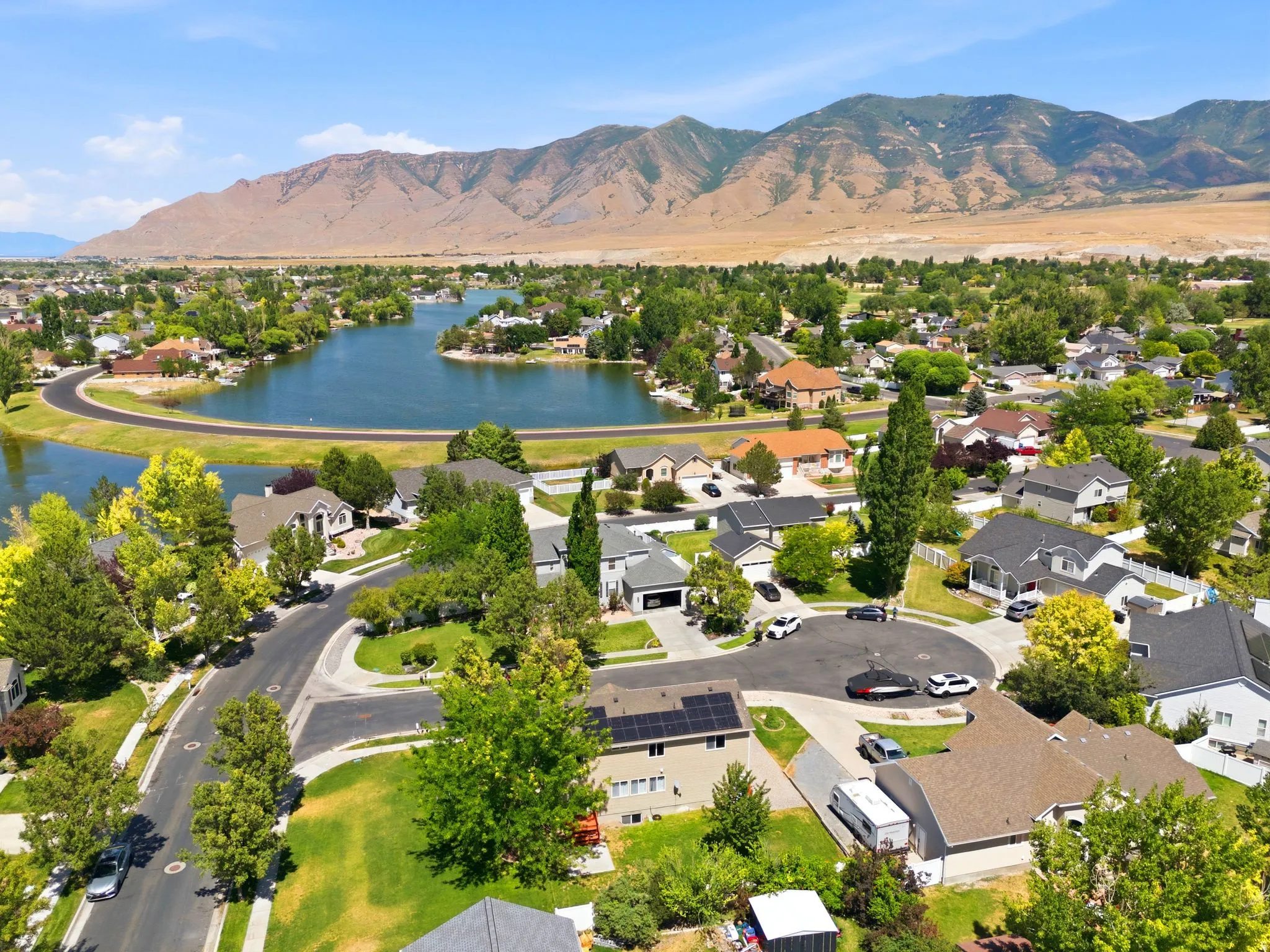 Residential neighborhood with a prominent lake feature, surrounded by mature trees and mountain scenery