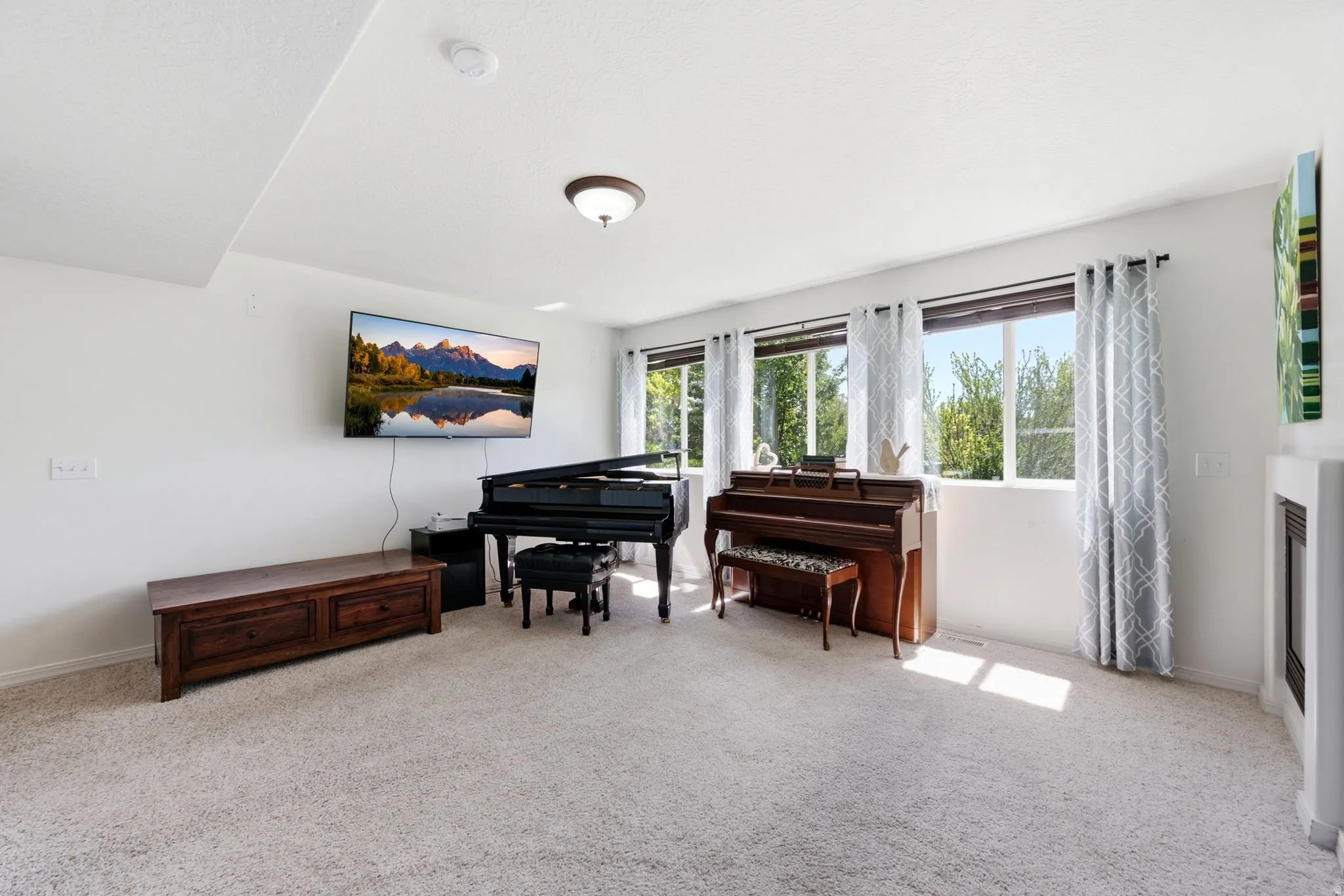 Carpeted living area featuring white walls, three windows with exterior landscaping visible, a ceiling-mounted light fixture, and a built-in fireplace