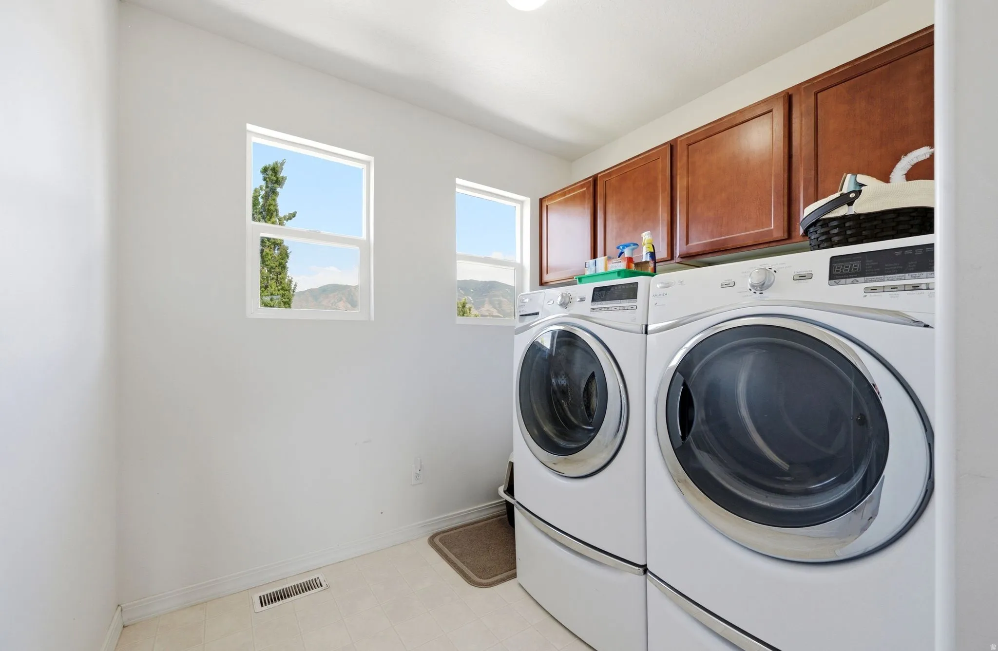Laundry area featuring two windows, overhead cabinetry with a wood finish, and light-toned flooring