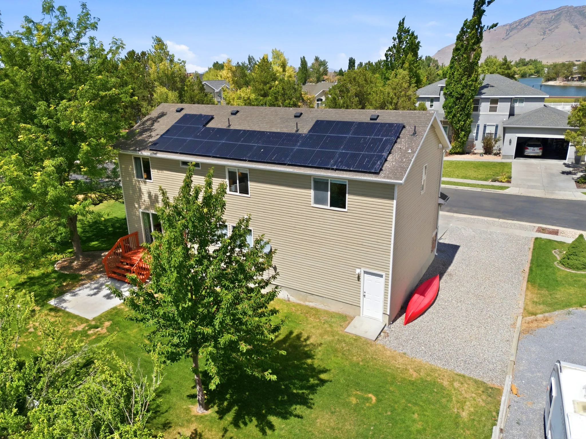 Rear elevation featuring solar panels, a multi-level deck, and a grass lawn with mature trees