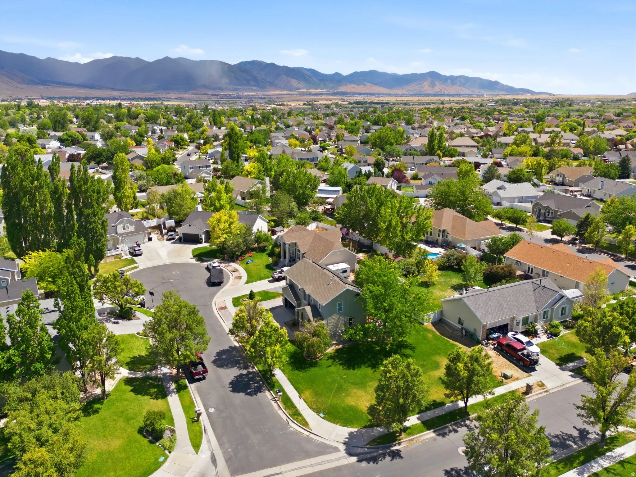 Residential neighborhood featuring mature trees, paved streets with sidewalks, and distant mountains