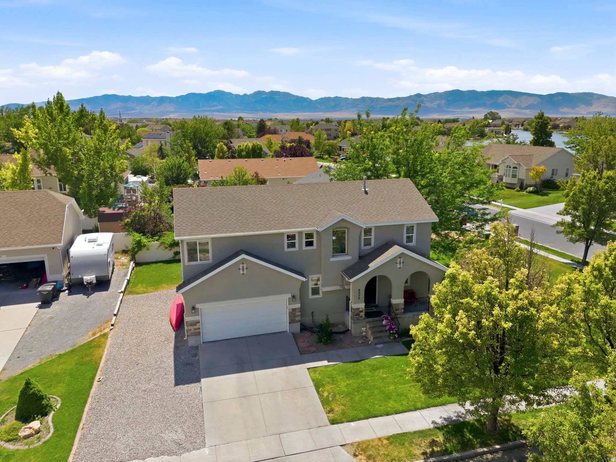 Two-story stucco residence featuring an attached two-car garage, stone accent siding, and a covered entry porch with arched supports