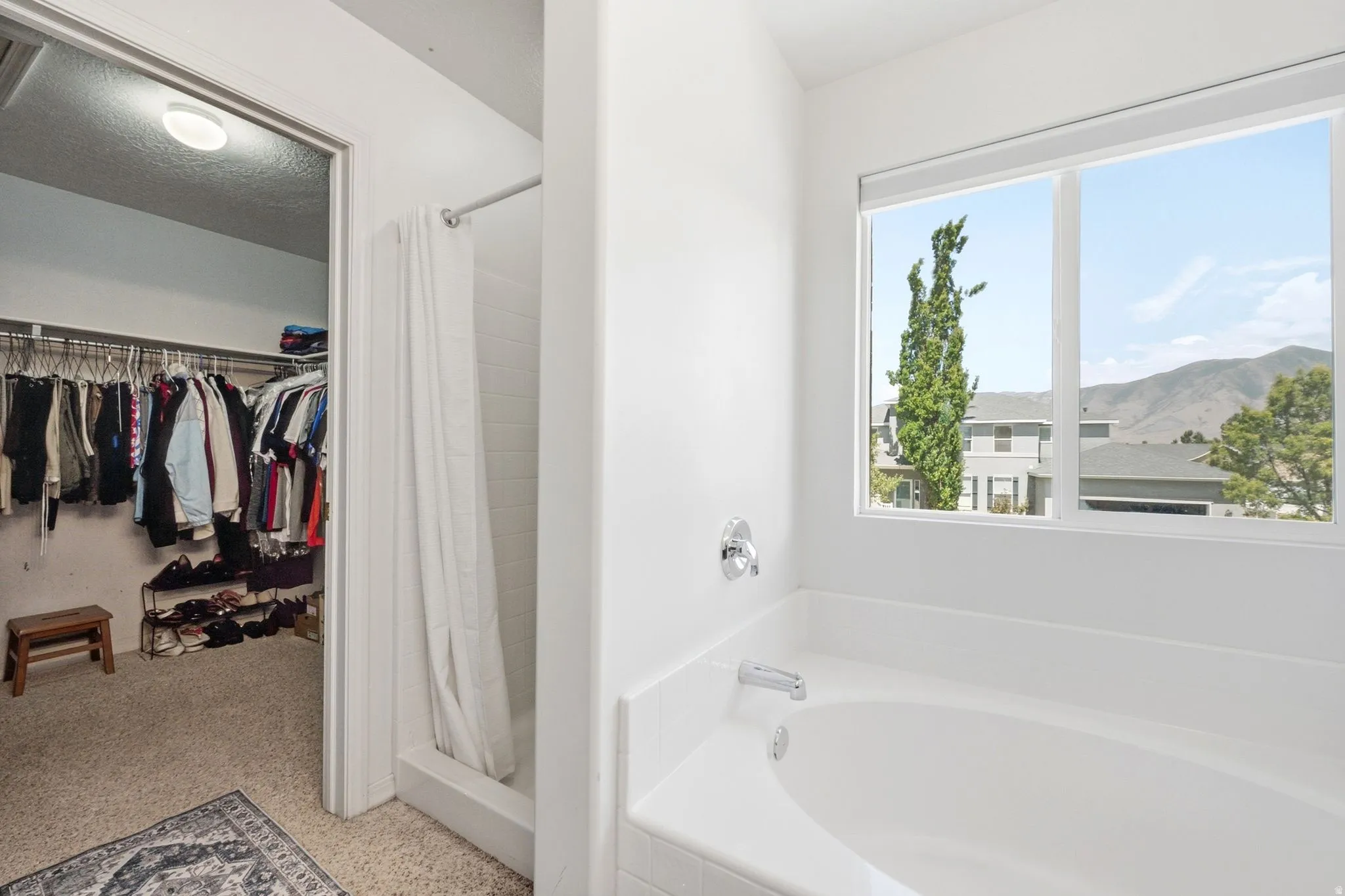 Bathroom featuring a spacious built-in soaking tub with chrome fixtures, a shower enclosure with a white subway tile surround, and a walk-in closet with carpet flooring and organized hanging racks