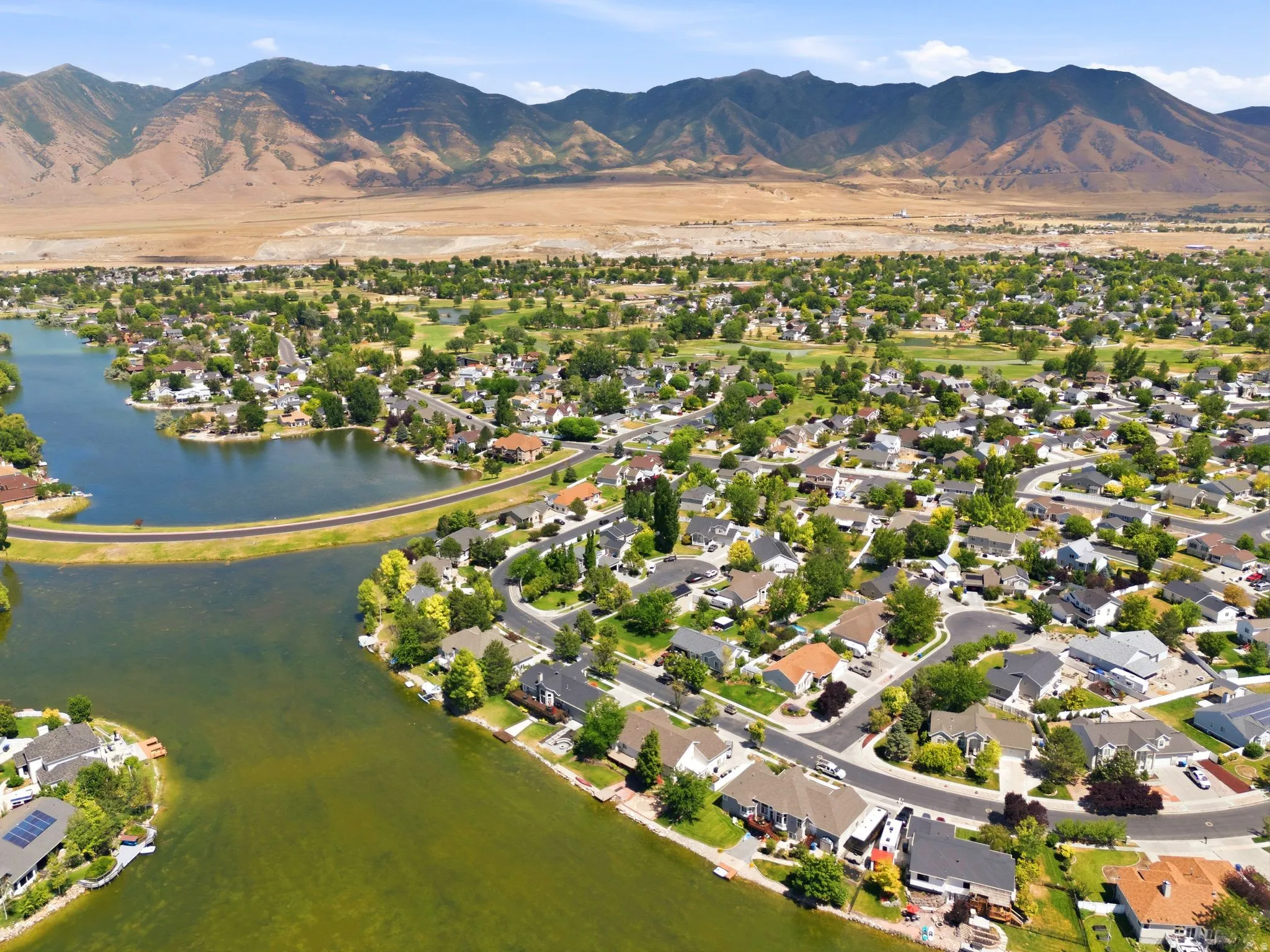 Expansive aerial perspective showcasing a residential community with a large body of water, established trees, and mountainous terrain in the background
