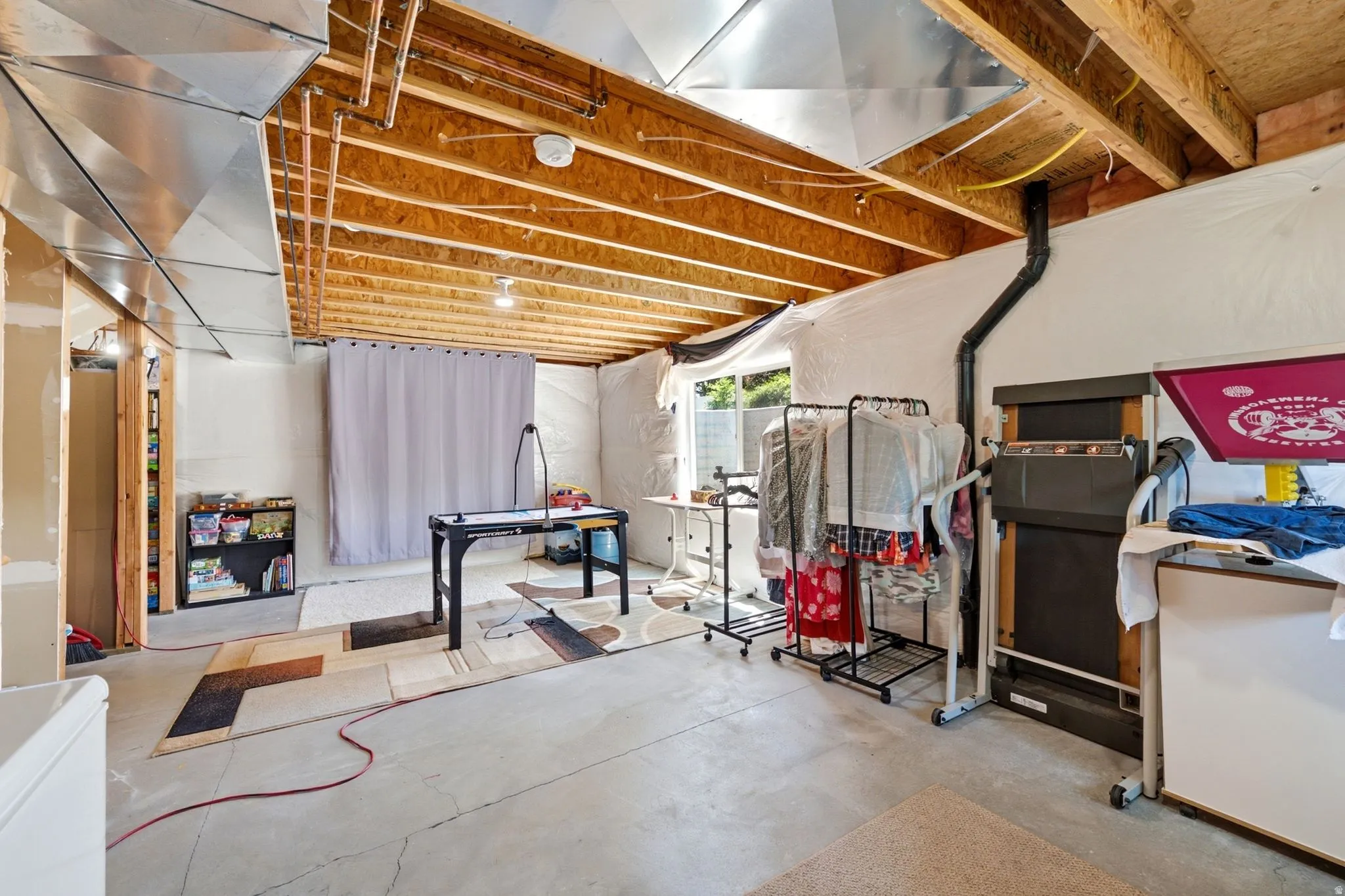 Unfinished basement space featuring exposed ceiling joists, concrete flooring, and a walk-out egress window