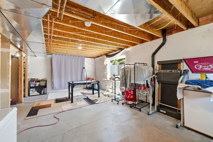 Unfinished basement space featuring exposed ceiling joists, concrete flooring, and a walk-out egress window
