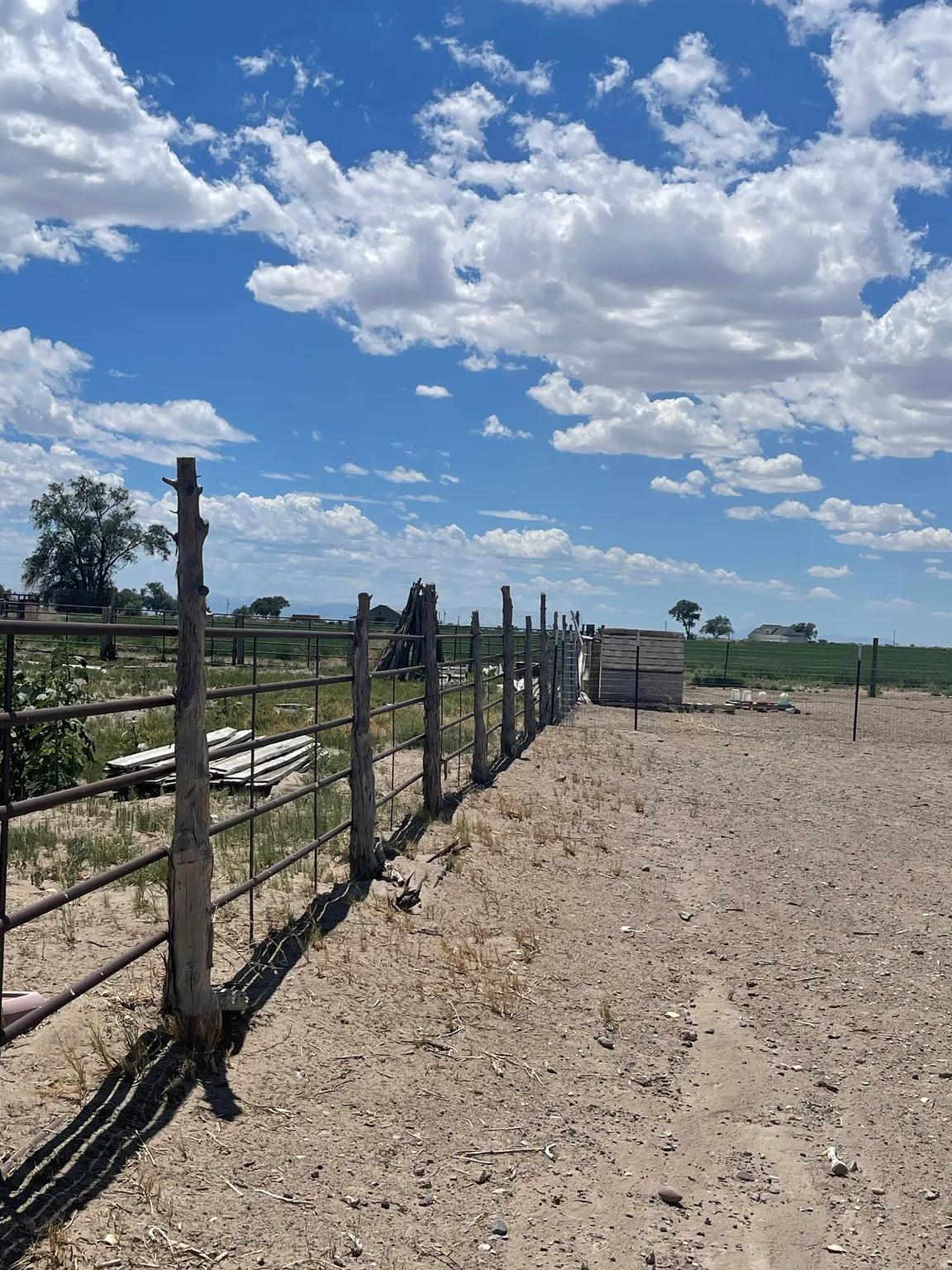 Fenced perimeter with metal paneling and rustic wooden posts, framing a parcel of land under a clear sky with scattered clouds