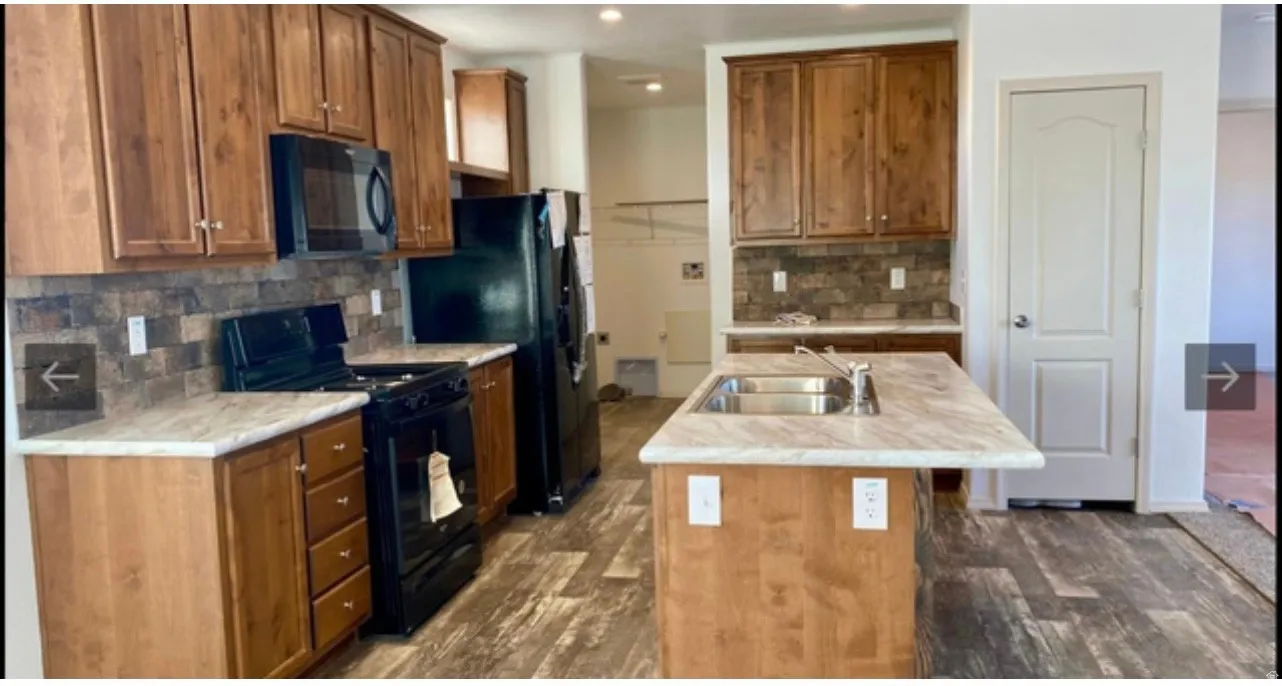 Kitchen featuring wood-finish cabinetry, black appliances, a central island with an undermount sink, and wood-finish flooring