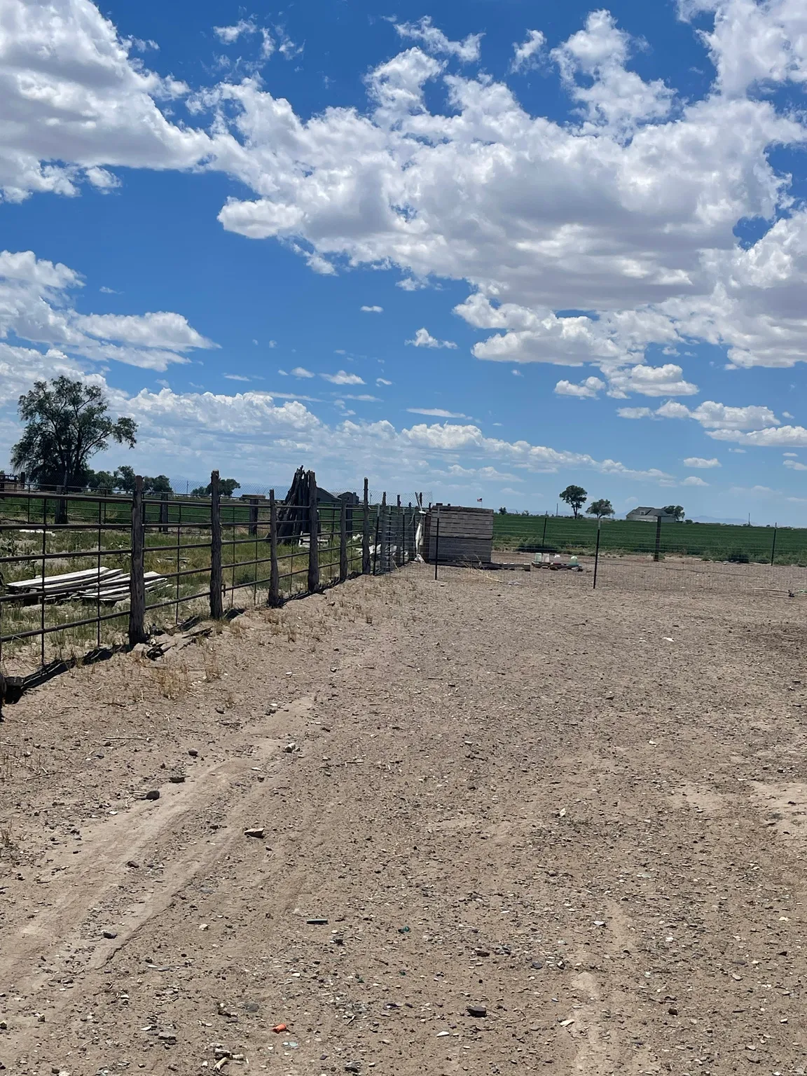 Expansive land parcel featuring a metal fence line, a small block structure, and a broad dirt surface