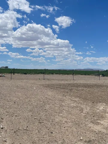 Expansive parcel featuring a cleared, level dirt surface, partial fencing, and distant green fields