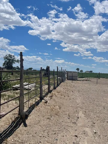 Fenced perimeter with metal paneling and rustic wooden posts, framing a parcel of land under a clear sky with scattered clouds