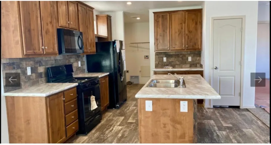 Kitchen featuring wood-finish cabinetry, black appliances, a central island with an undermount sink, and wood-finish flooring