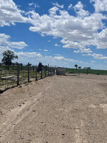Expansive land parcel featuring a metal fence line, a small block structure, and a broad dirt surface