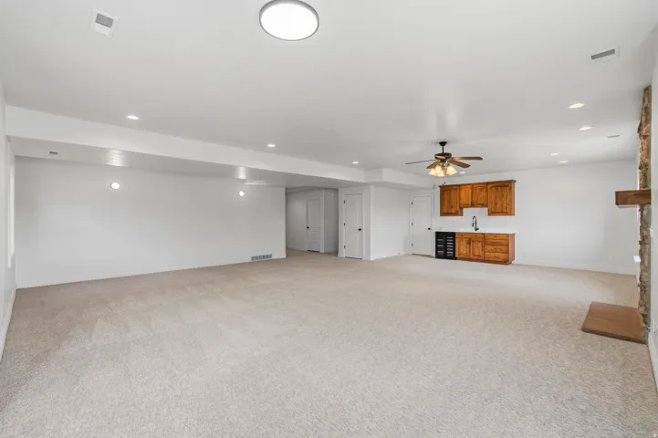 Spacious room featuring light-colored carpeting, recessed lighting, and a prominent wet bar with wood cabinetry and a beverage cooler