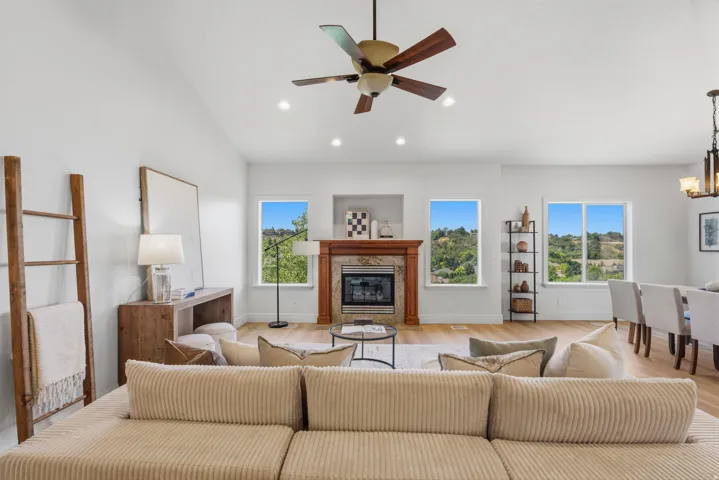 Vaulted ceiling living area featuring a fireplace with a wood-finish mantel and tile surround, recessed lighting, and a multi-blade ceiling fan