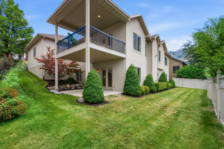 Rear exterior featuring a covered upper-level balcony, a lower-level patio, and a manicured lawn