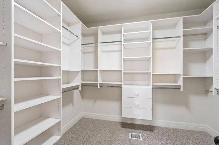 Walk-in closet featuring extensive built-in shelving, multiple hanging rods, three integrated drawers, and neutral carpeting