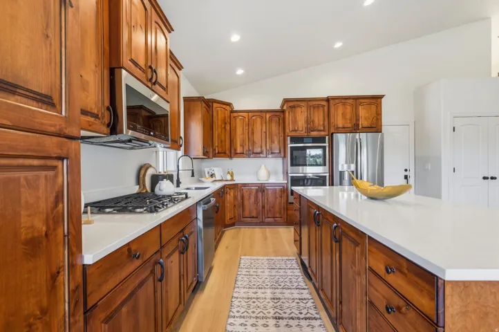 Spacious kitchen featuring warm wood cabinetry with dark hardware, white countertops, and a full suite of stainless steel appliances