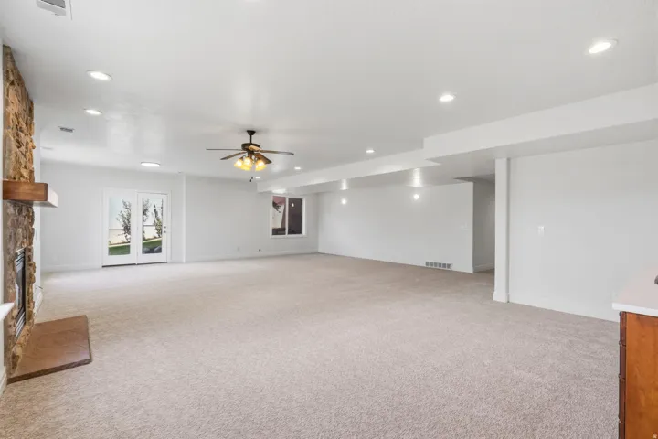 Spacious room featuring light-toned carpeting, a stone-clad fireplace with a wood mantle, and recessed ceiling lighting