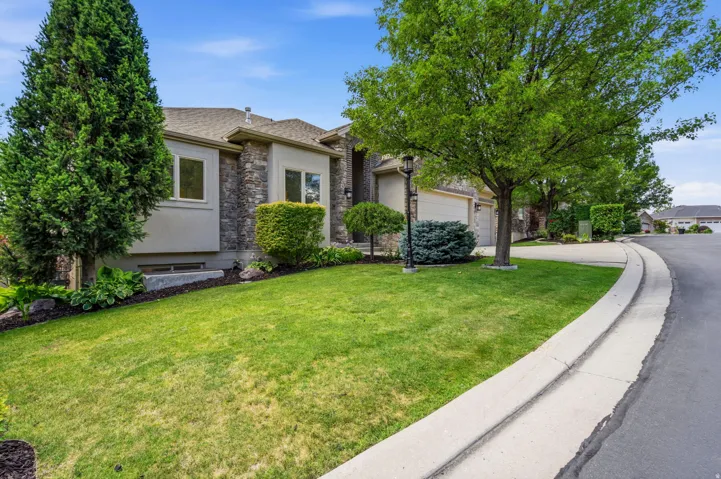Exterior featuring a stone and stucco facade, a two-car garage, mature trees, and landscaping with shrubs and ground cover