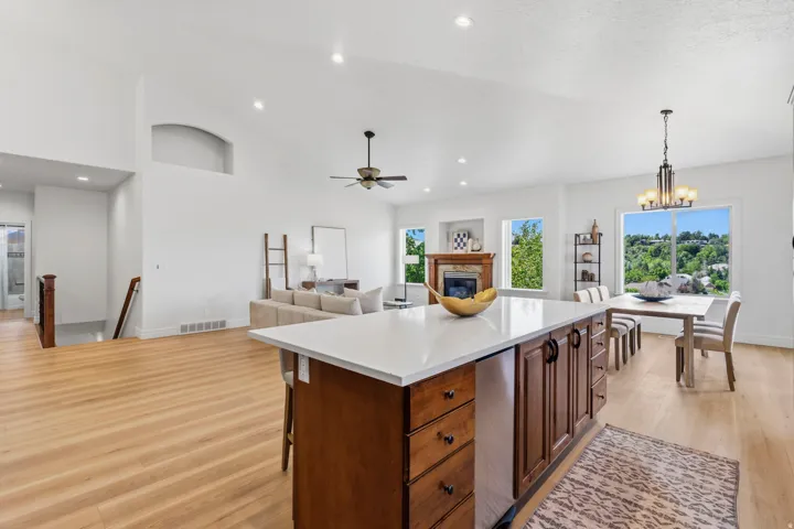 Spacious open-concept living area featuring wood-finish flooring, vaulted ceilings, recessed lighting, and a kitchen island with a light-toned countertop and dark wood cabinetry