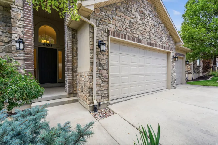 Stone and brick veneer exterior featuring a two-car garage, arched entry with a dark paneled door, sidelights, and exterior sconce lighting